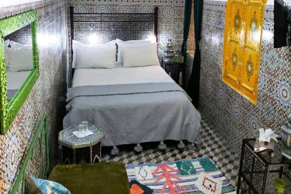 Un dormitorio con una cama, una mesita pequeña, un espejo y una lámpara colgante.