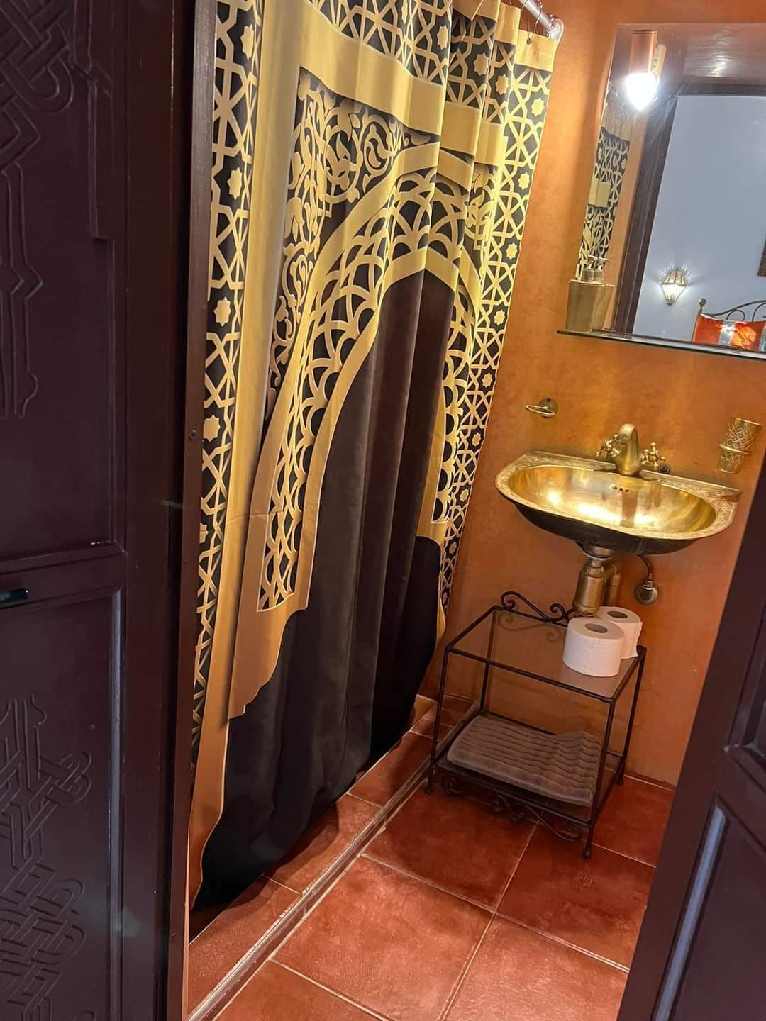 A bathroom with a decorative curtain, a sink with a mirror, and a small shelf with toiletries.