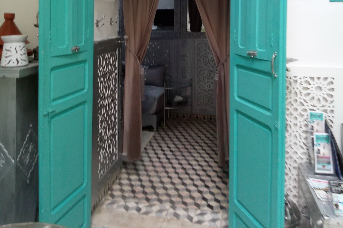 Un umbral abierto que da a una habitación con baldosas estampadas, un sofá y un techo decorativo.