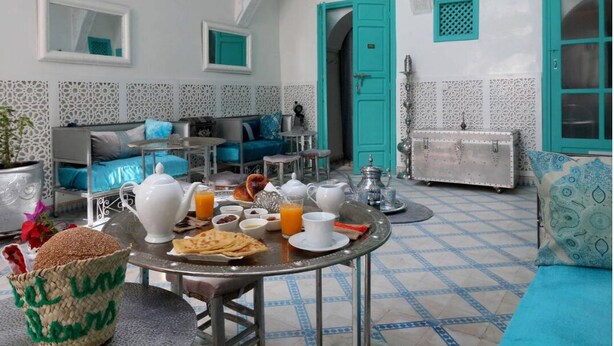 Un comedor con una mesa lista para el desayuno, que incluye pan, huevos y jugo. Hay un sofá y un armario al fondo.