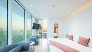 A modern hotel room with a large bed, a sofa, a TV, and a city view.