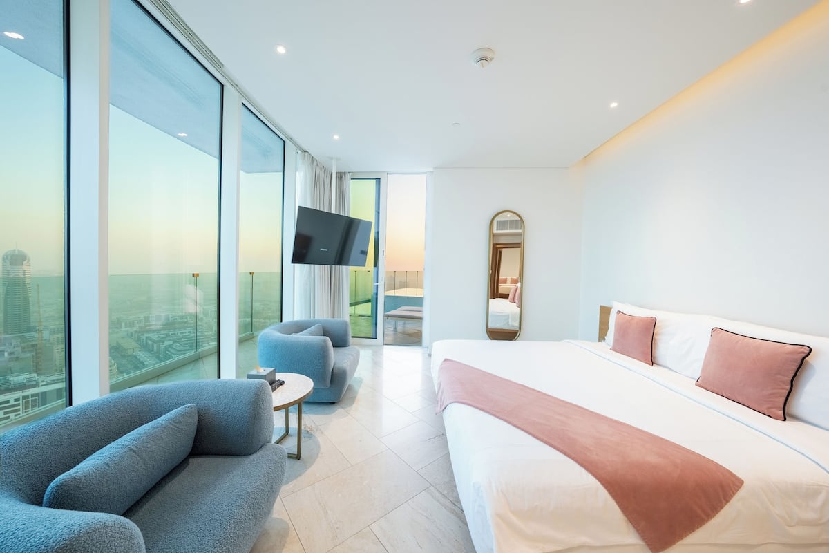 A modern hotel room with a large bed, a sofa, a TV, and a city view.
