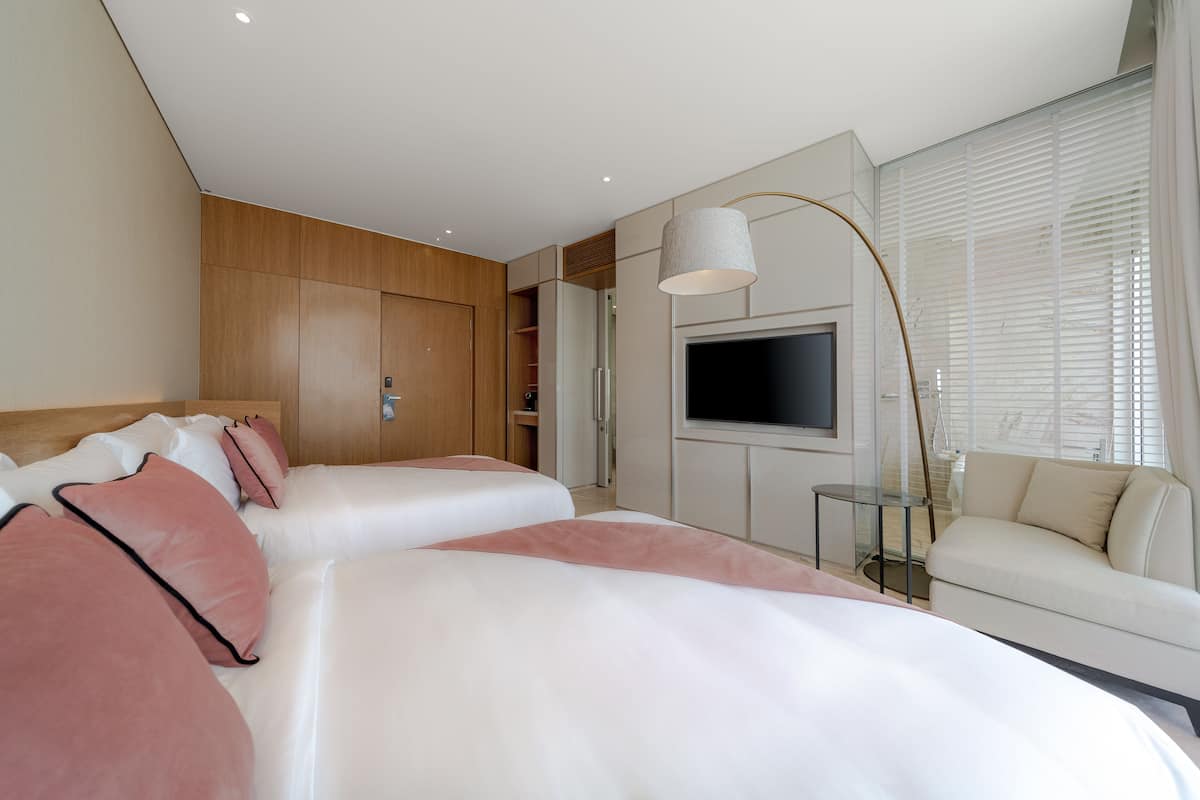 A modern hotel room with a large bed, a TV, a sofa, and a glass table.