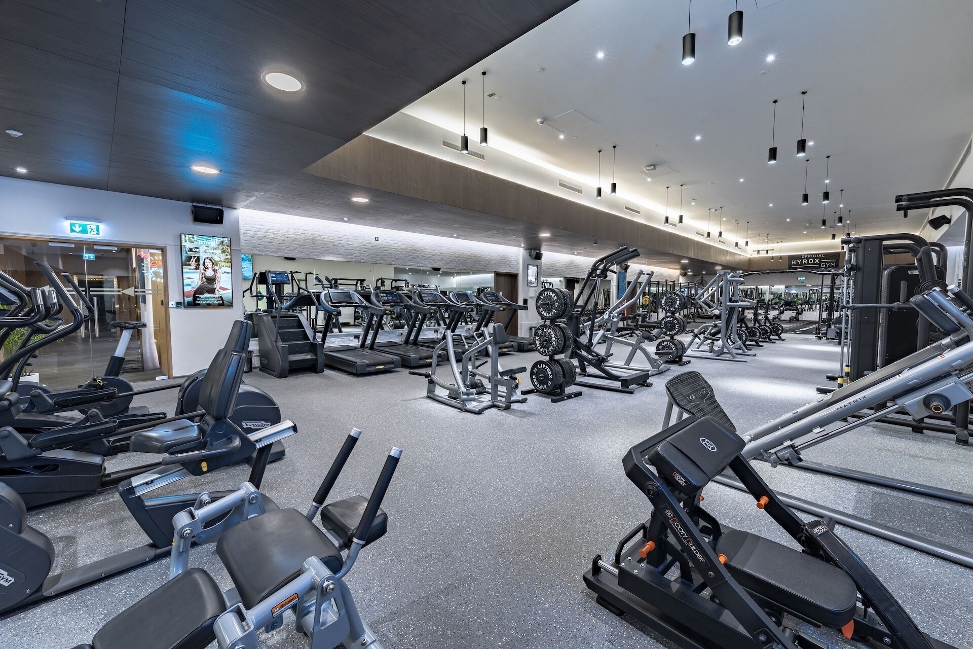 A gym with various exercise equipment, a mirrored wall, and a ceiling with recessed lighting.