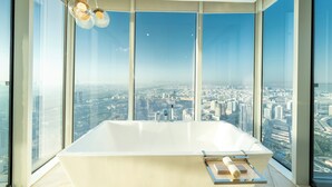 A modern bathroom with a large bathtub, a view of a cityscape through large windows, and a hanging light fixture.
