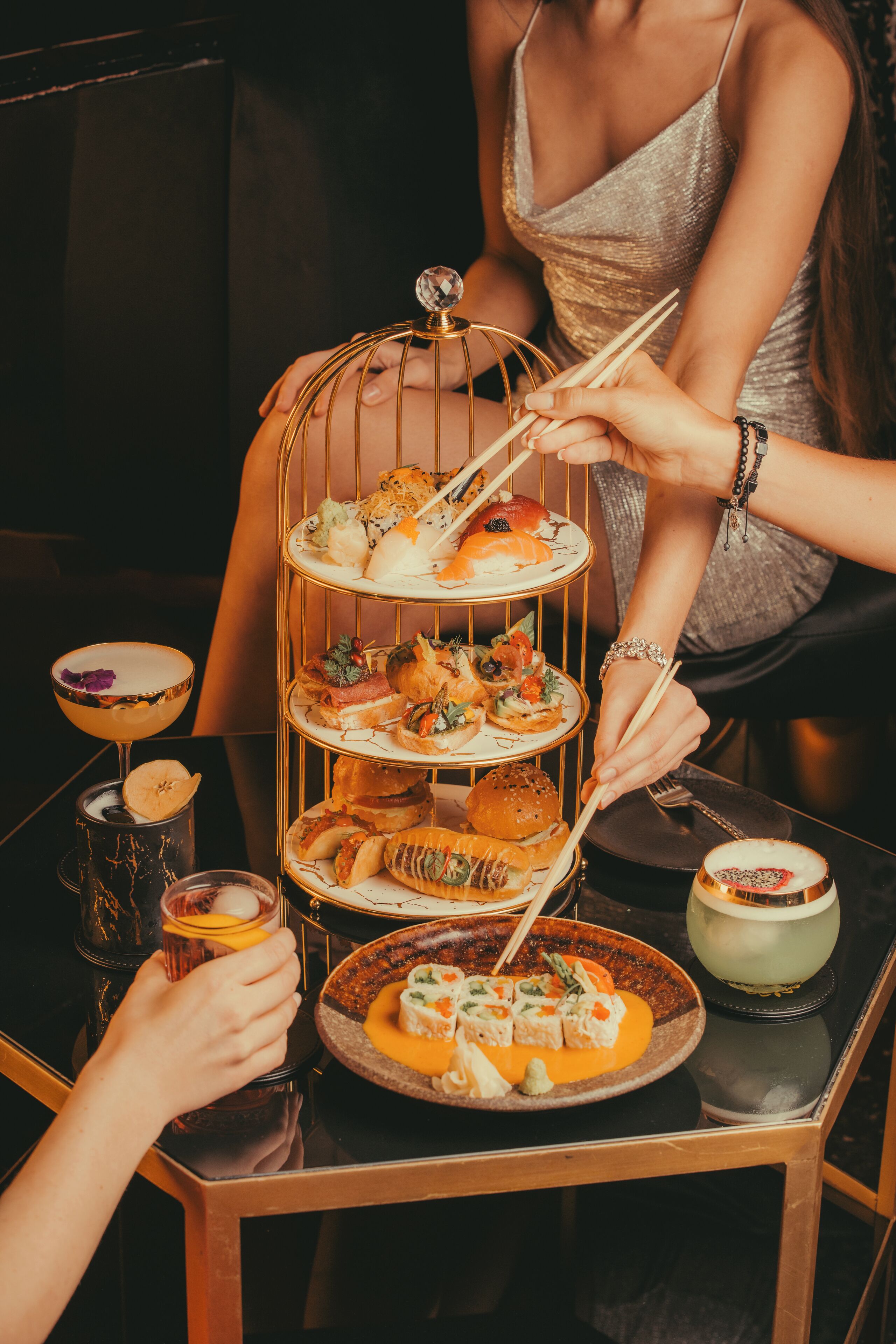 Un soporte escalonado para postres con varios pasteles y un cóctel sobre una mesa.