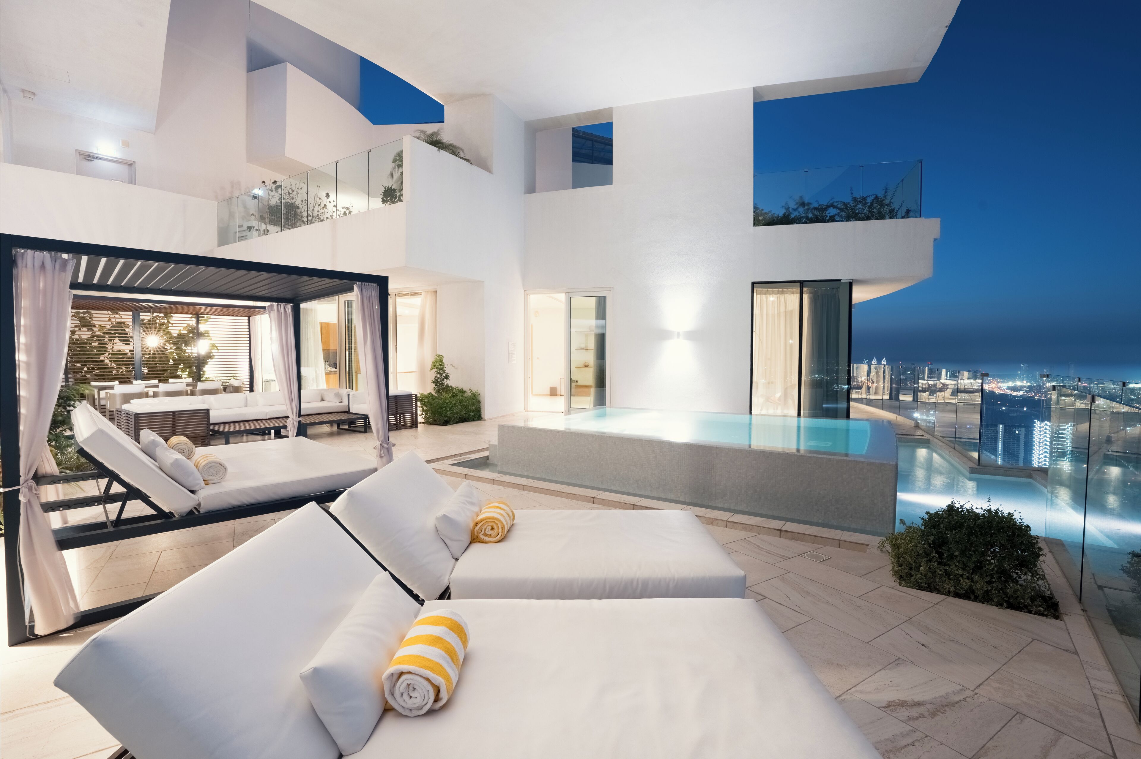 Un espace piscine moderne aménagé sur le toit, avec des chaises longues et une balustrade en verre offrant une vue sur le paysage urbain.
