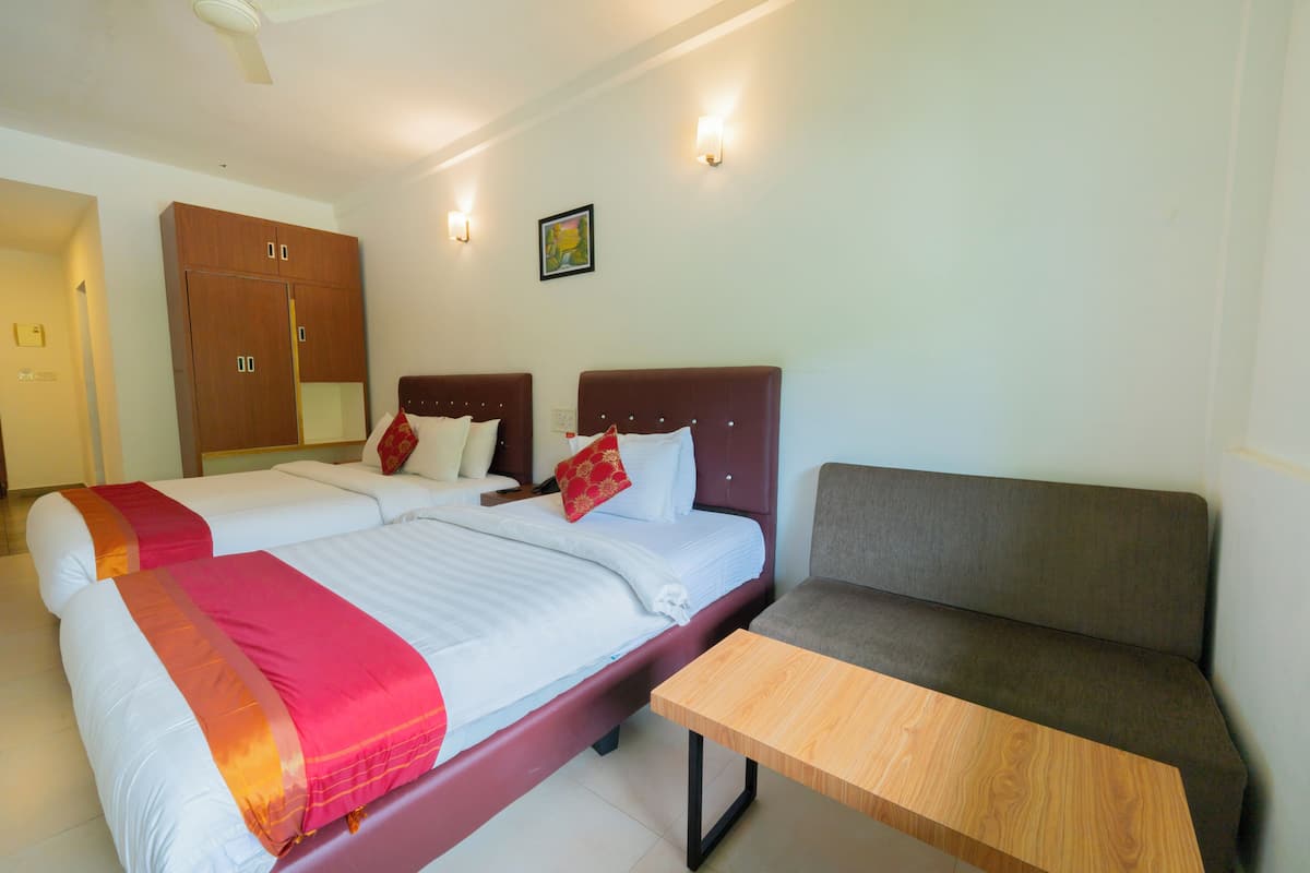 A hotel room with two beds, a sofa, a wooden table, and a ceiling fan.
