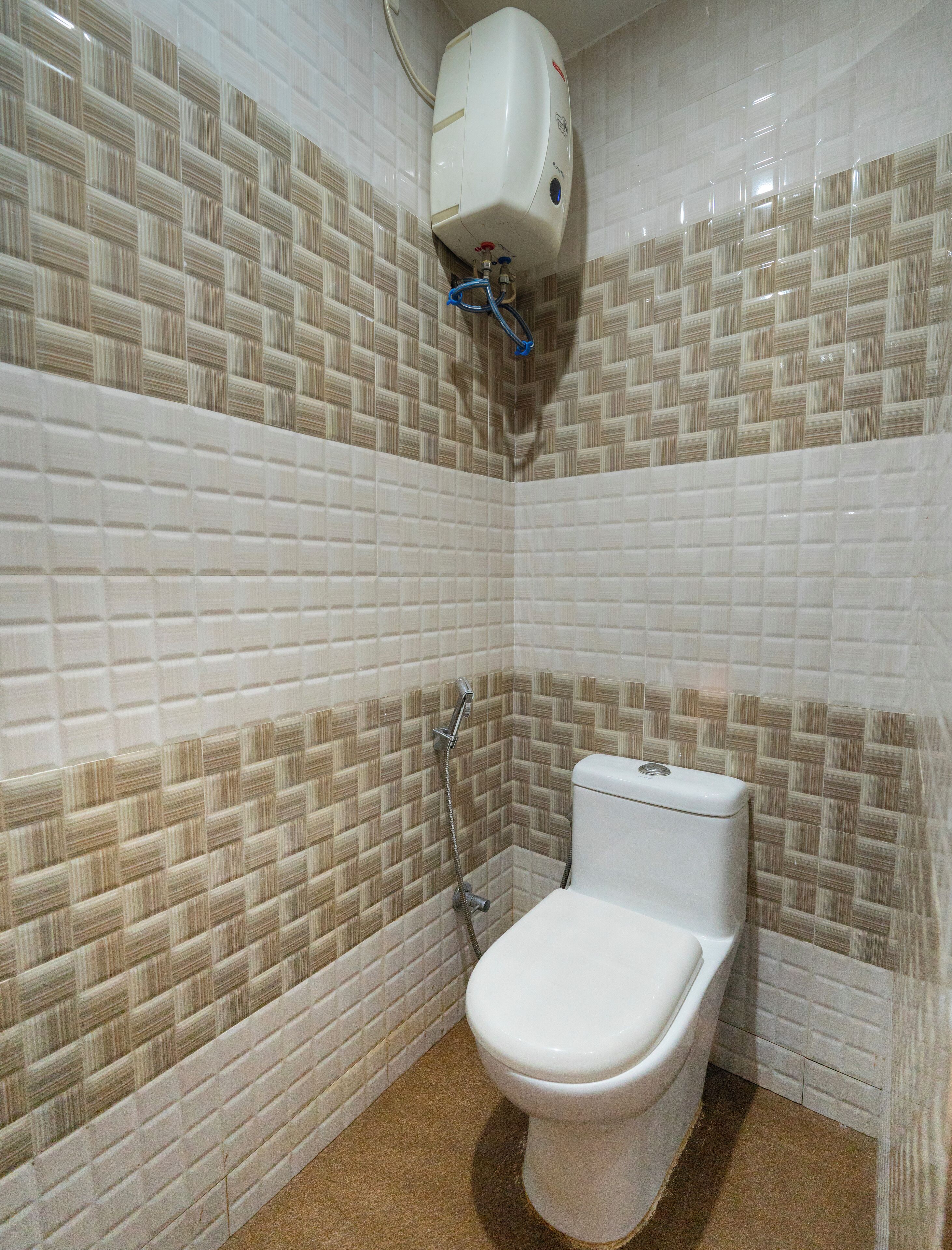 Un baño con inodoro, ducha de mano y dispensador de jabón en la pared.