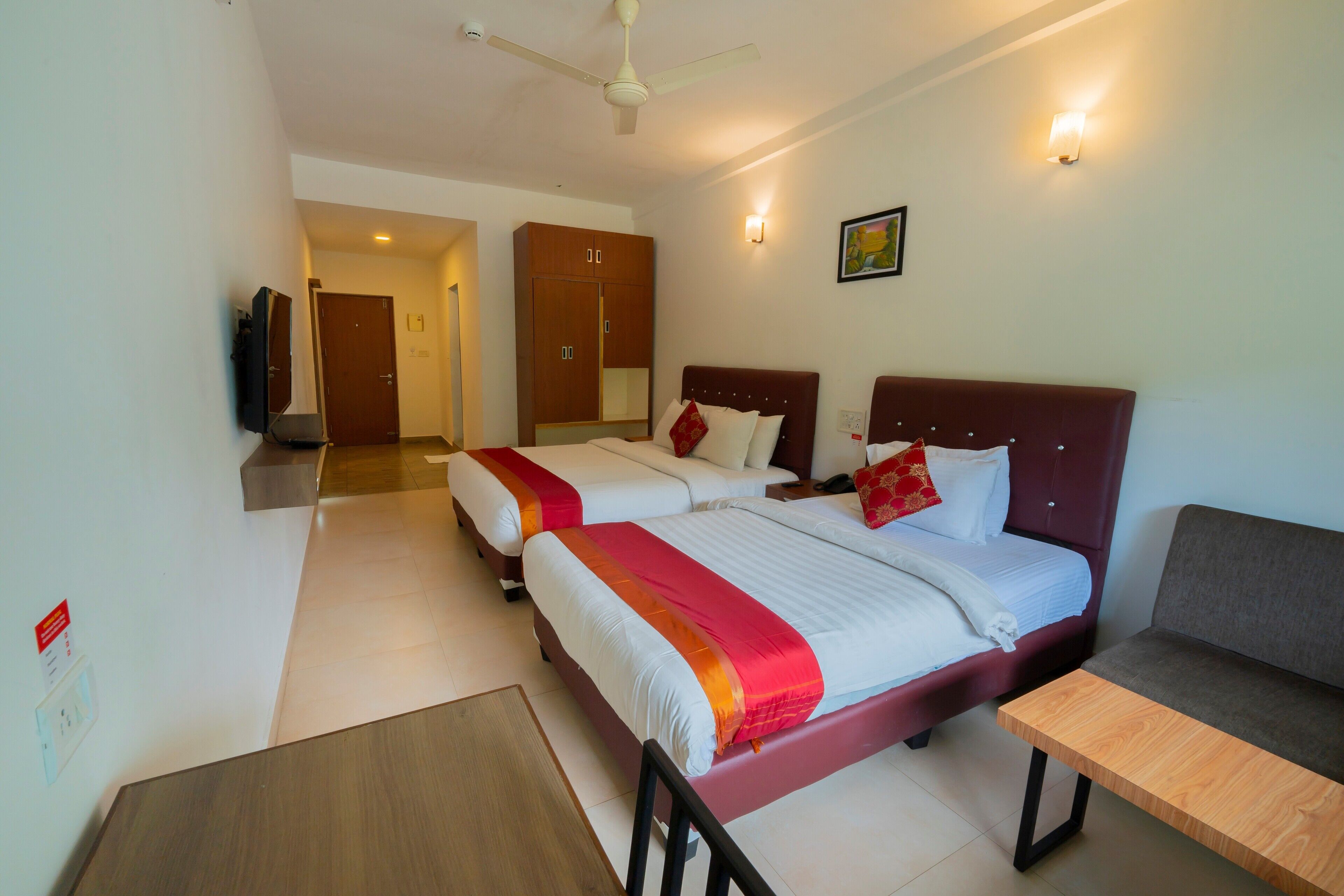 A hotel room with two beds, a sofa, a table, and a ceiling fan.