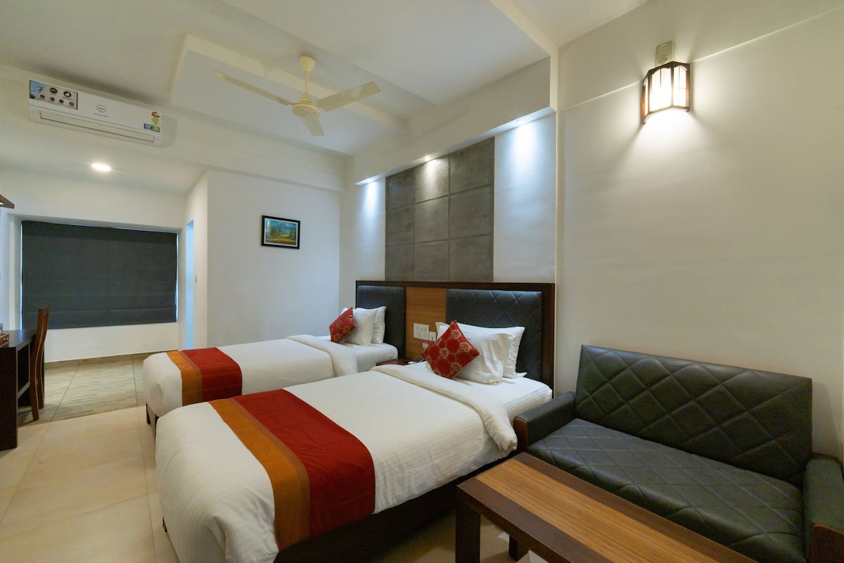 A hotel room with two beds, a sofa, a desk, and a ceiling fan.