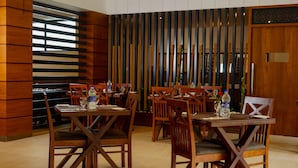A dining area with wooden tables and chairs, a decorative wall with vertical slats, and a wooden door. - The Sanihara Hotel & Resort (Vythiri)
