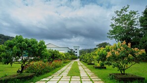 A pathway leading to a building with a modern design, surrounded by lush greenery and trees. - The Sanihara Hotel & Resort (Vythiri)