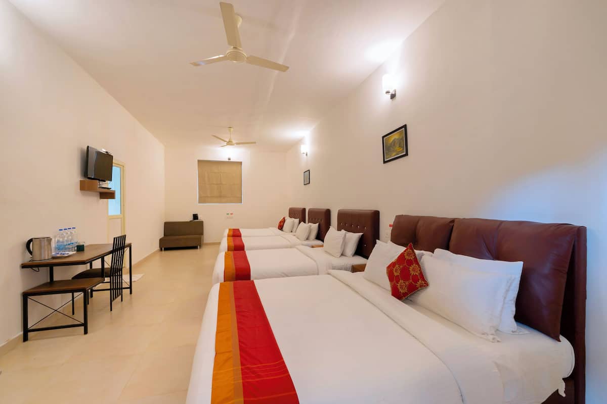 A hotel room with four beds, a desk with chairs, a television, and ceiling fans.