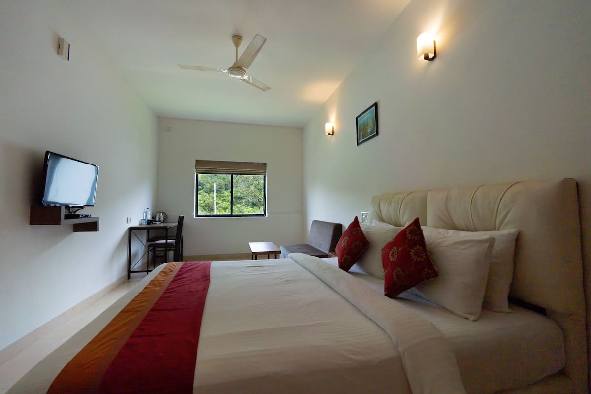 A hotel room with a bed, a desk, a chair, a television, and a window.