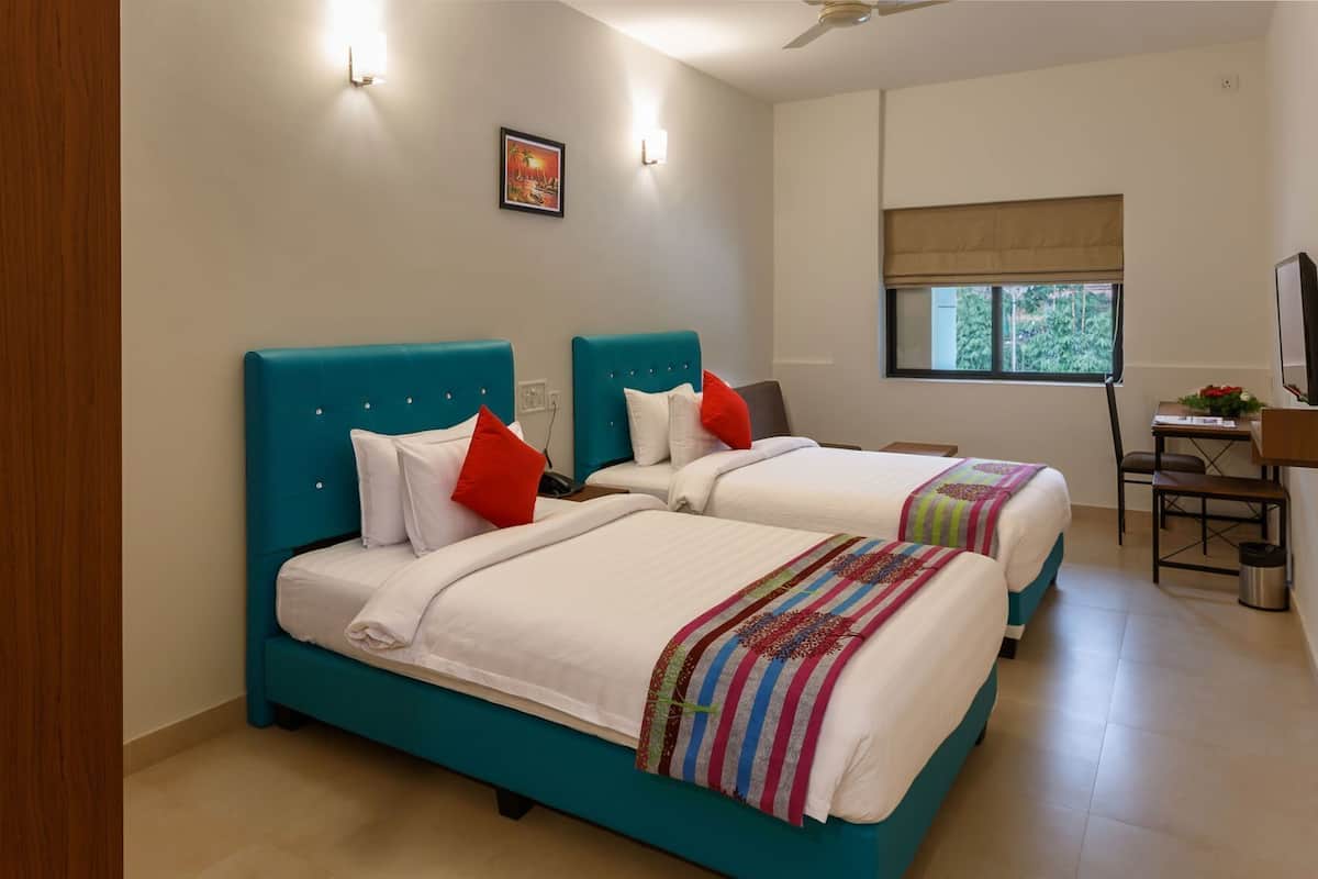 A hotel room with two beds, a desk, a chair, a window with a view, and a ceiling fan.