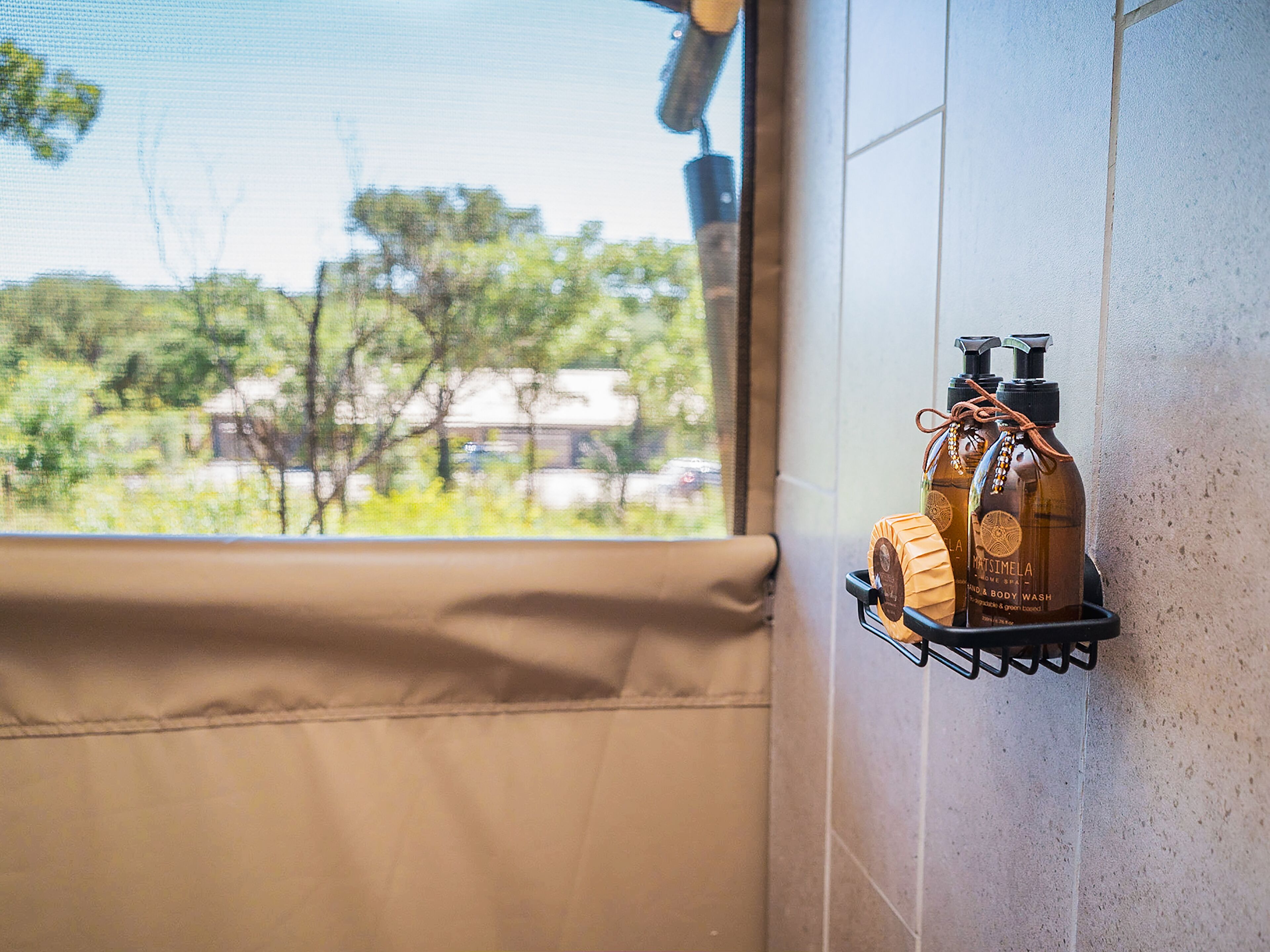 Un baño con vista a la ventana, un perchero con botellas y una toalla color beige.