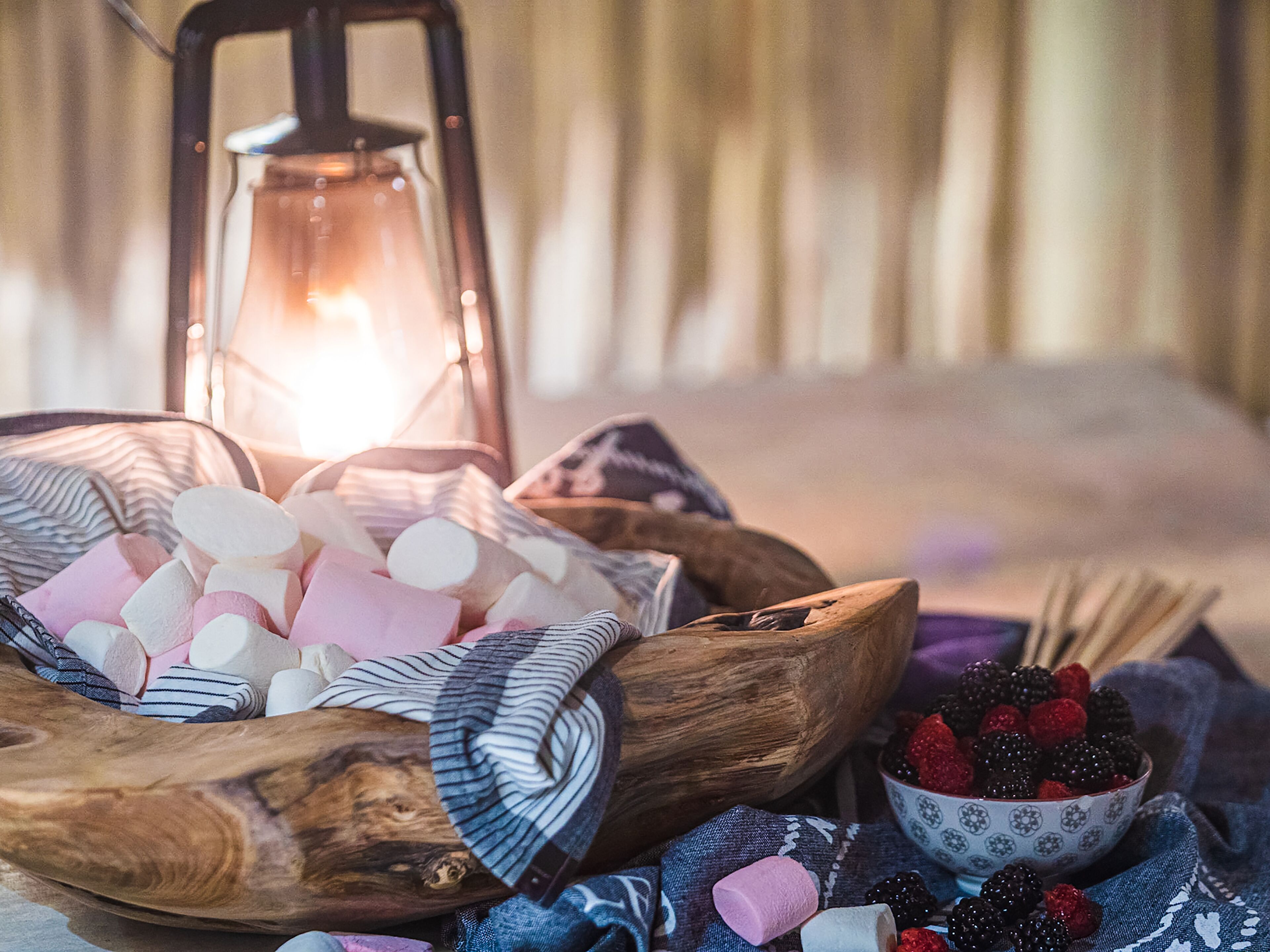 Een houten schaal gevuld met marshmallows en een schaal bessen op een tafel met een gestreepte tafelkleed.