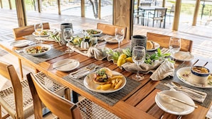 Une table à manger dressée avec des assiettes, des couverts, des verres et une variété de plats, donnant sur un espace extérieur pittoresque.