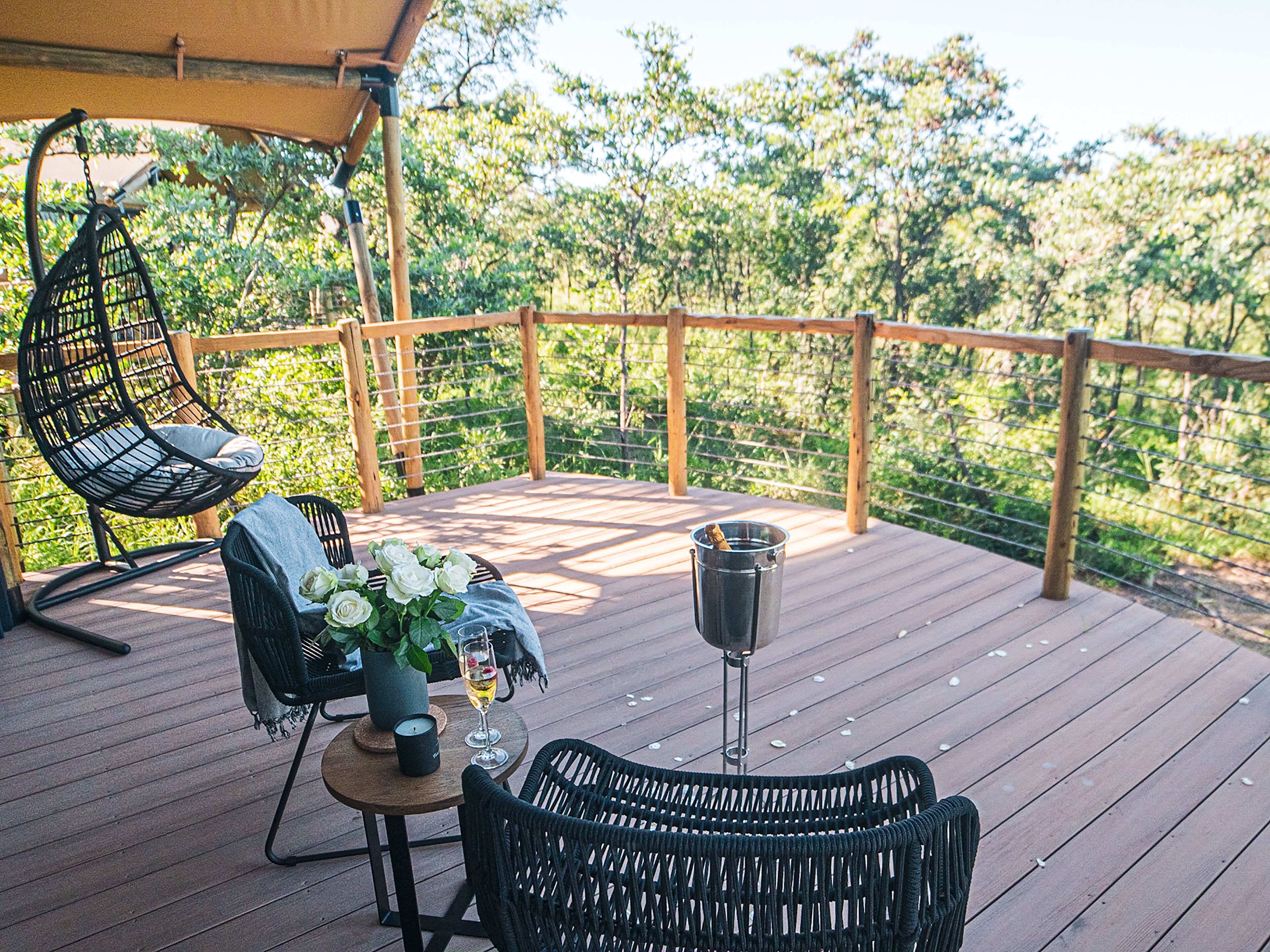 Une terrasse en bois avec des chaises en osier, une table avec une bougie et un verre de vin.
