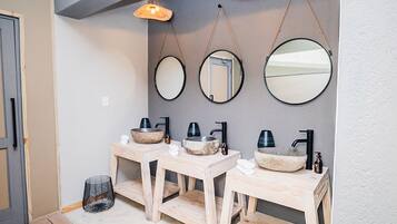 A bathroom with three wooden vanity units, each with a stone basin and black faucets. There are three wall-mounted mirrors and two hanging woven light fixtures.