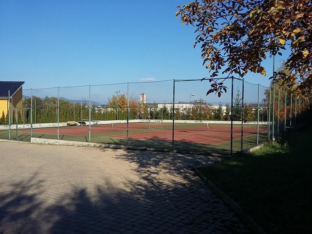 Ein Sportplatz mit Zaun, Bäumen und einem Gebäude im Hintergrund.