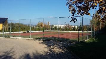 Ein Sportplatz mit Zaun, Bäumen und einem Gebäude im Hintergrund.