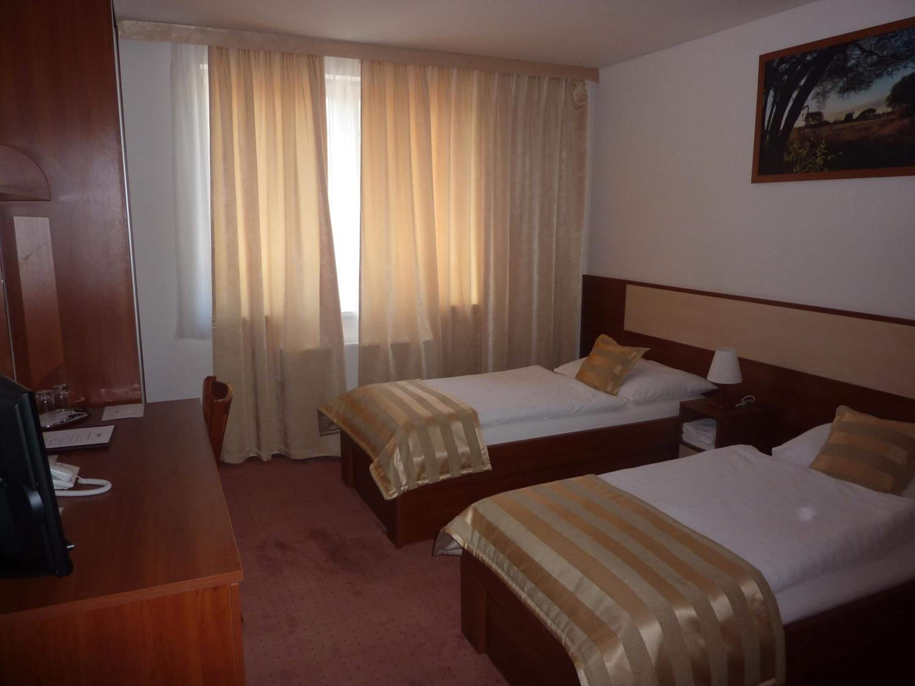 Een hotelkamer met twee bedden, een bureau met telefoon en een raam met gordijnen.