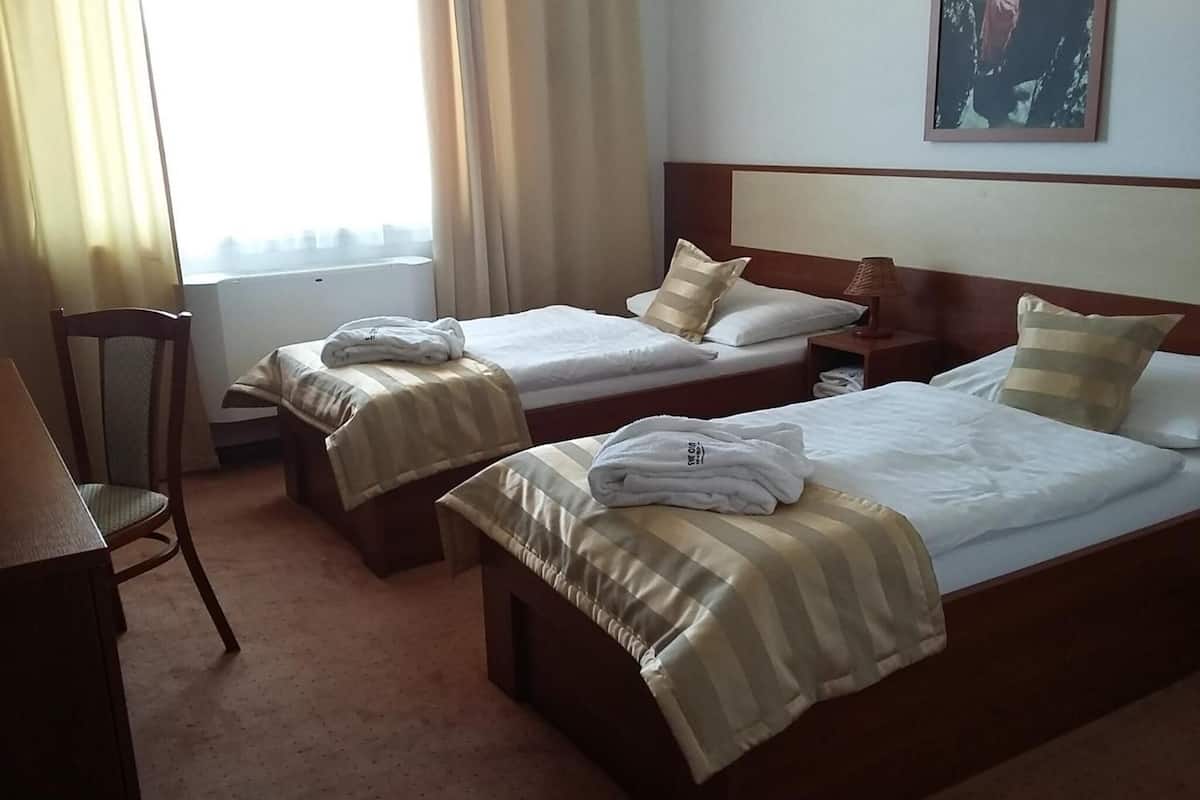A hotel room with two single beds, a wooden nightstand, a chair, and a window with curtains.