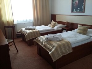 A hotel room with two single beds, a wooden nightstand, a chair, and a window with curtains. - Hotel Auto Jas (Nitra)