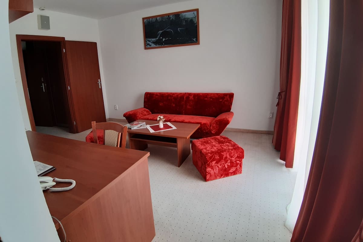 A room with a red sofa, a wooden table, a small ottoman, a painting on the wall, and a door.