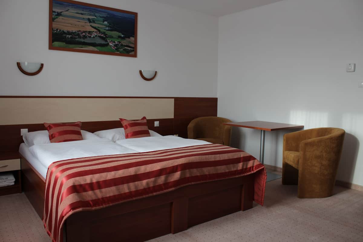 A hotel room with a large bed, a desk, two chairs, and a painting on the wall.