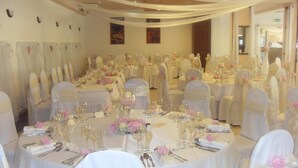 A banquet hall with round tables set for a formal event, each with white tablecloths, silverware, and pink floral centerpieces. - Hotel Auto Jas (Nitra)
