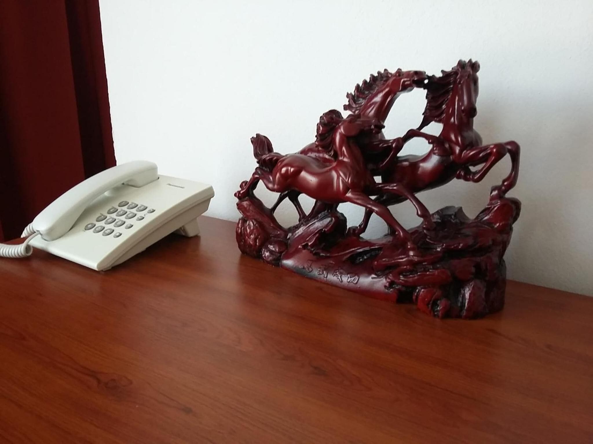 A wooden desk with a white telephone and a red horse sculpture.