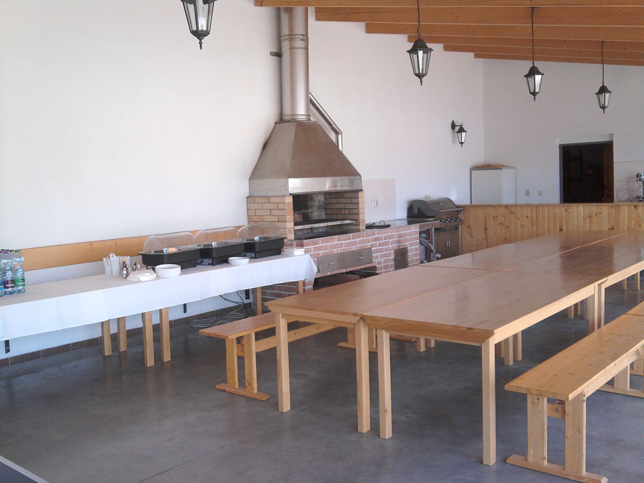 A long wooden table with benches, a brick oven, and a grill in a spacious indoor area.