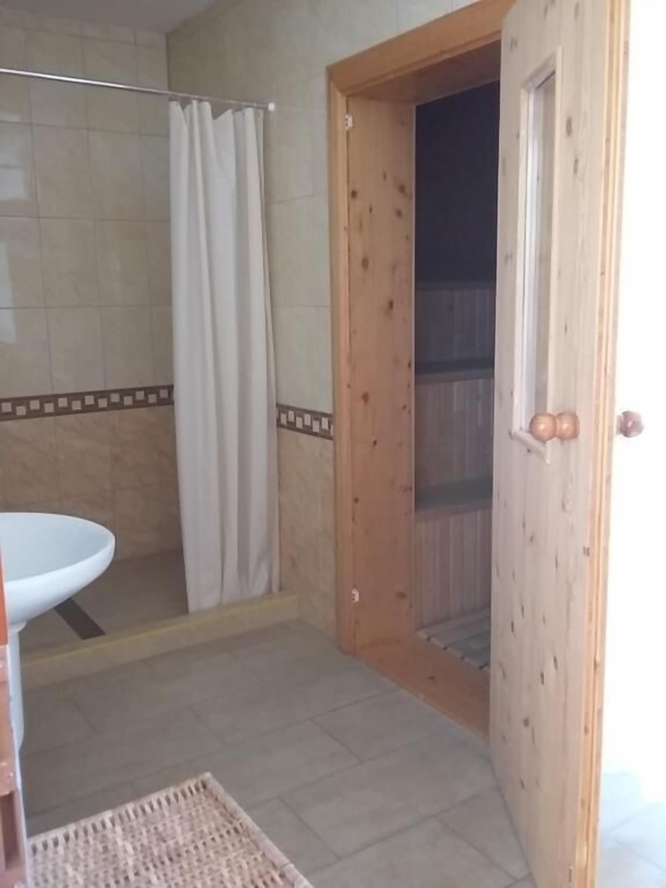 Un bagno con doccia, lavandino e una porta in legno che dà su un balcone.