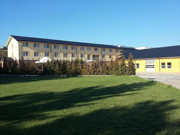 A multi-story building with a flat roof, a well-maintained lawn, and a clear sky. - Hotel Auto Jas (Nitra)