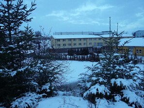 A building with multiple windows and a flat roof, surrounded by snow-covered trees and a clear sky. - Hotel Auto Jas (Nitra)