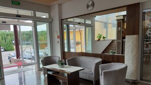 A lobby with a reception desk, seating area, and a view of the outside. - Hotel Auto Jas (Nitra)
