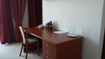 A wooden desk with a telephone, a decorative item, and a tray with glasses in a room with a chair and a red curtain.