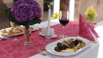 A table set with a candle, a glass of red wine, and a plate of food.