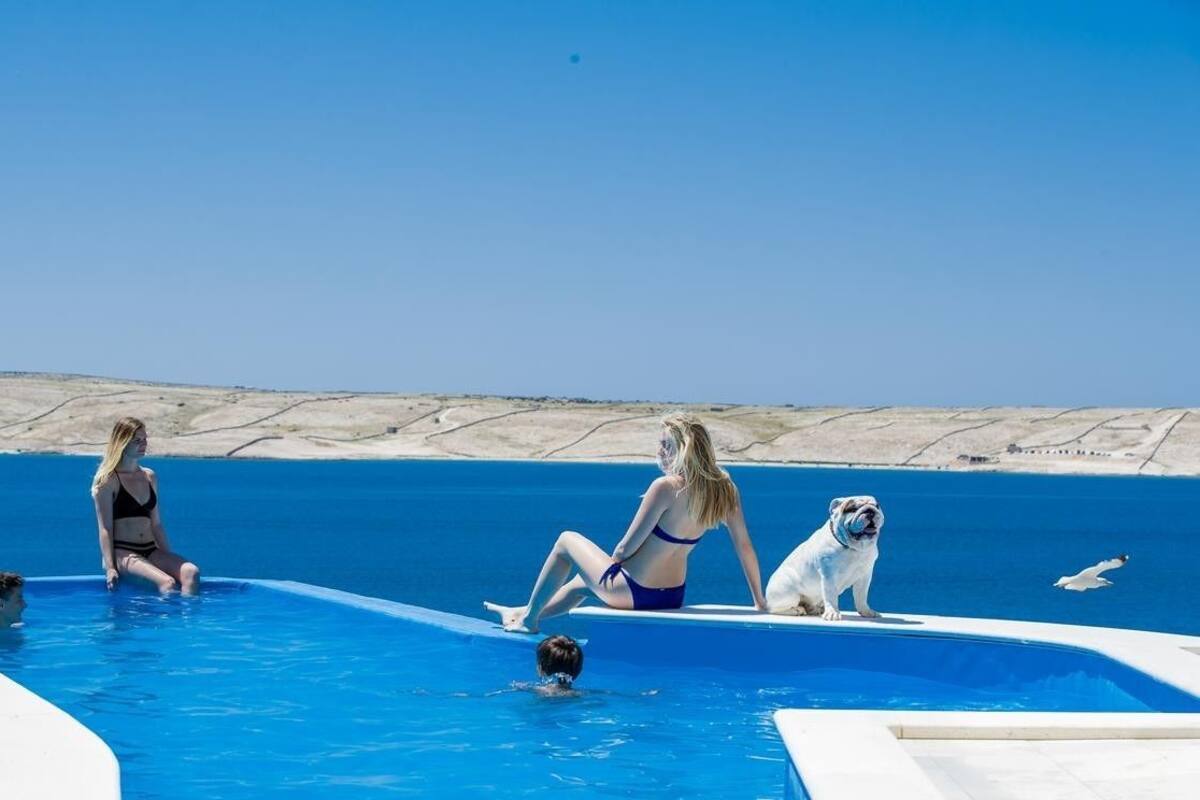 A pool area with a clear blue sky, a white pool edge, and a sandy landscape in the background.