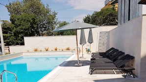 A swimming pool with lounge chairs and umbrellas, surrounded by a tiled patio and a low wall. - Abalone Apartments (Crikvenica)