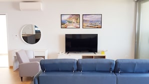 A modern living room with a blue sofa, a flat-screen TV, and two framed paintings on the wall. - Abalone Apartments (Crikvenica)