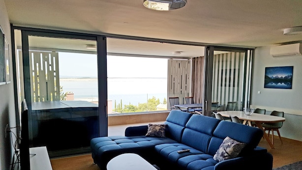 A modern living room with a blue sofa, a small table, and a view of the sea through large glass doors. - Abalone Apartments (Crikvenica)