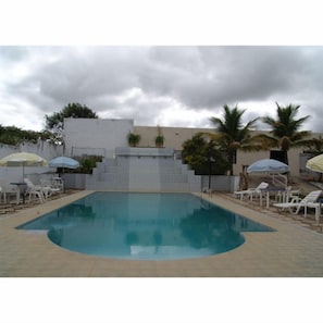 A rectangular swimming pool with a tiled deck, surrounded by white lounge chairs and striped umbrellas.