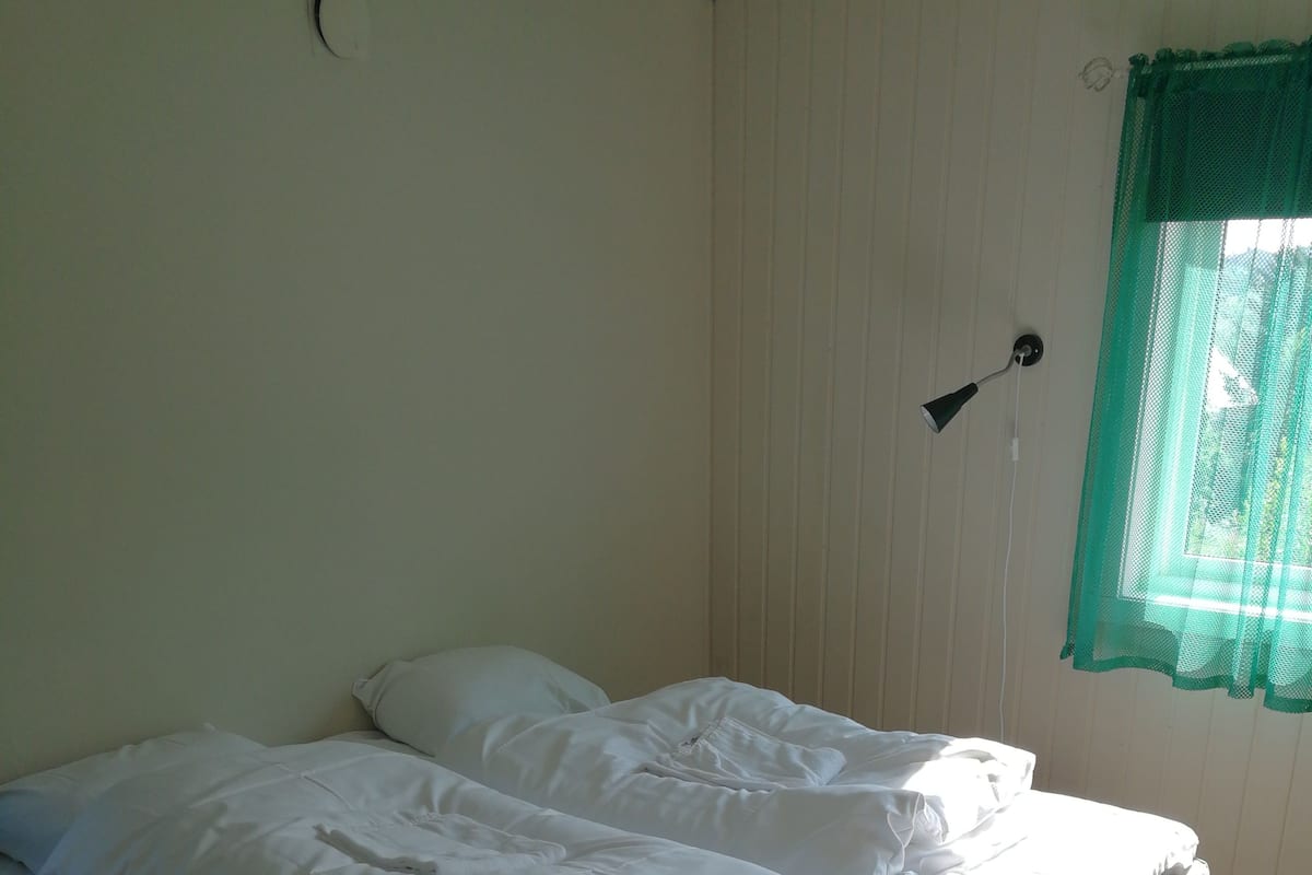 Una cama individual con ropa de cama blanca en una habitación con suelo de madera y persiana verde.