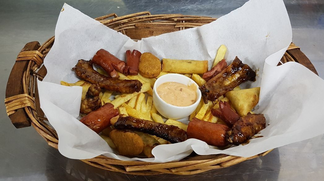 A basket containing various fried foods, including sausages, fries, and a small bowl of dipping sauce.