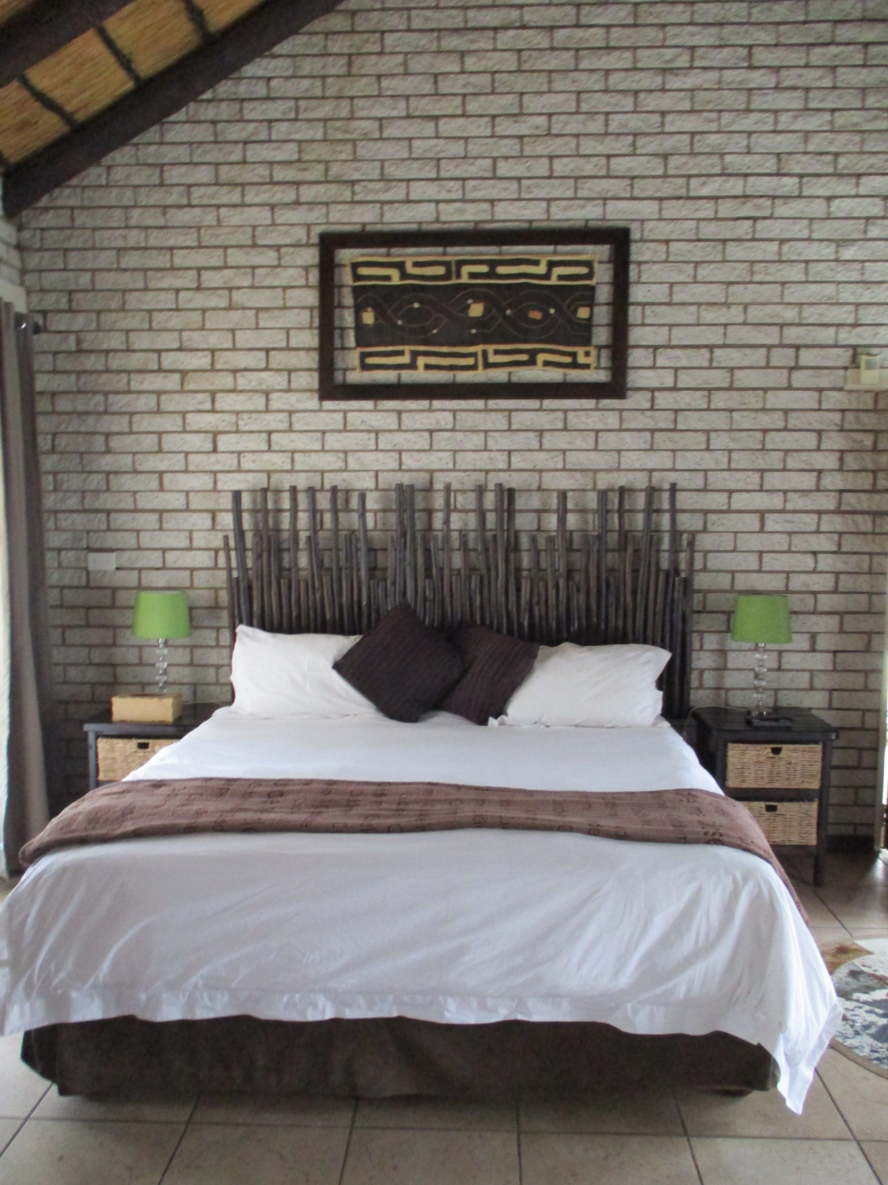 A bed with a white and brown bedspread, two pillows, and a headboard with a decorative pattern. There are two nightstands with lamps on either side of the bed.