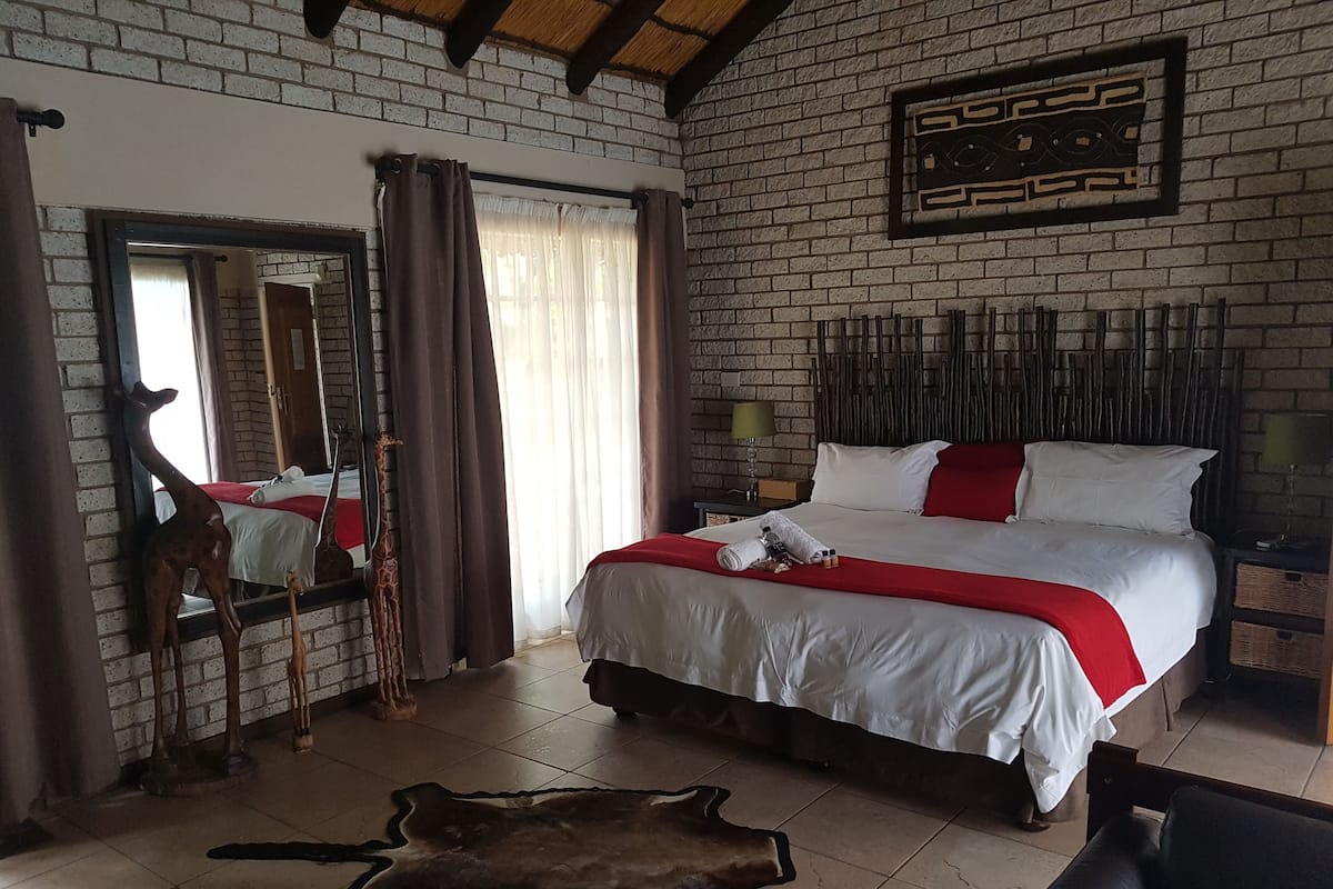 A bedroom with a large bed, a mirror, a giraffe sculpture, and a leather rug.